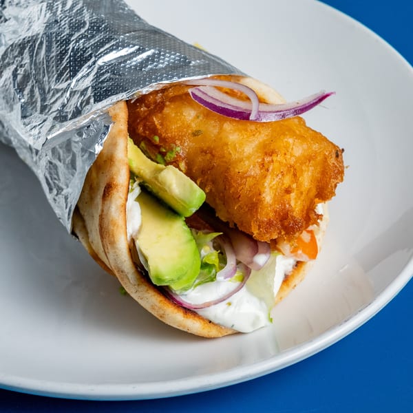 A Pita Press Greek Rotisserie pita wrap with fried fish, avocado, red onion, and sauce.