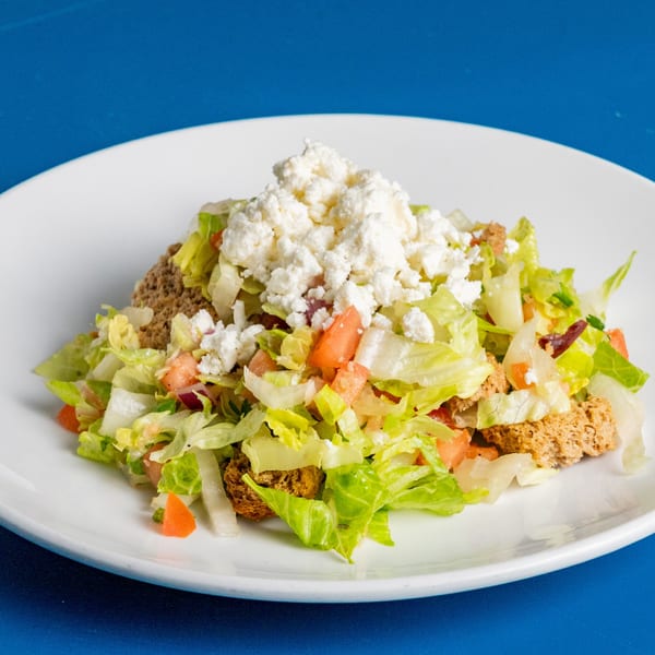 A fresh Greek salad with lettuce, tomatoes, and feta cheese on a white plate.