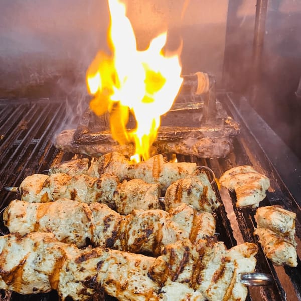 Chicken souvlaki skewers grilling over an open flame at Pita Press Greek Rotisserie.