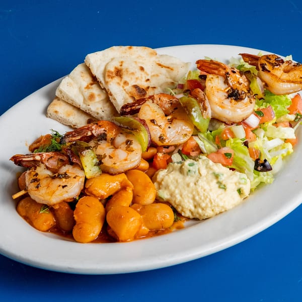 Grilled shrimp skewers, giant beans, hummus, salad, and pita bread on a white plate.